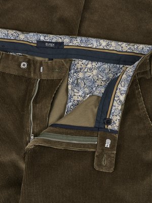 Nahaufnahme einer braunen Cordhose mit geöffnetem Reißverschluss. Der Hosenbund ist mit Paisley-Stoff gefüttert. Ein Knopf und das EUREX-Etikett sind sichtbar. Die Hose hat vertikale Streifen.