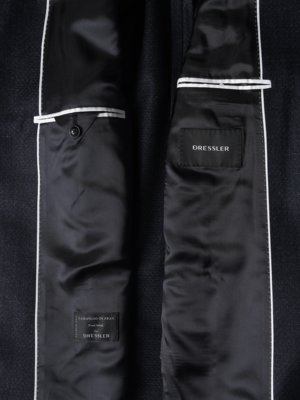 Blick in das Innere eines dunklen Sakkos mit schwarzem Seidenfutter und weißen Paspelierungen, sichtbare Taschen.