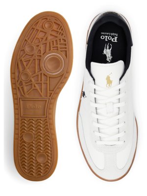 Zwei Ansichten von Polo-Sneakern. Der rechte Schuh zeigt weißes Leder, Schnürsenkel, einen schwarzen Fersenkragen und ein goldfarbenes Logo. Der linke Schuh zeigt die braune Sohle mit verschiedenen Mustern.