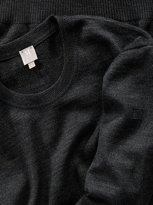 Draufsicht auf einen dunkelgrauen Pullover. Links oben ist der Rundhalsausschnitt zu sehen, darunter ein Etikett. Auf dem Ärmel ist ein kleines Logo zu erkennen. Der Stoff wirkt fein.