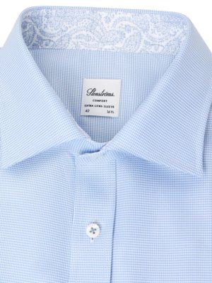 Close-up of a light blue dress shirt with a small checkered pattern. The collar is folded down with a white and blue paisley design. A white tag reads "Stenströms Comfort Extra Long Sleeve 42 16 1/2". One white button is fastened.