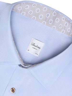 Close-up of a light blue button-down shirt. The collar is detailed with a decorative patterned lining. A tag on the inside collar shows the brand name "Stenströms", along with size information: 45, Comfort, and 17 3/4. A gold-toned button is visible.