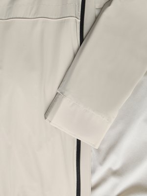Ein Ausschnitt eines hellbeigen Kleidungsstücks mit einem schwarzen Streifen an der Seite und einem Ärmelabschluss.