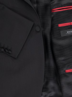Close-up of a black suit jacket. The jacket has a buttoned cuff with three buttons and a single button on the lapel. The interior lining of the jacket is black with red trim, and a label that reads "DIGEL."