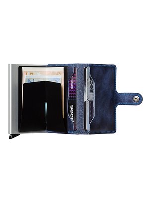 A partially open blue leather wallet, with a metal card holder to the left. The wallet holds paper money, two credit cards, and is secured with a snap closure. The brand "secrid" is visible on the cards.