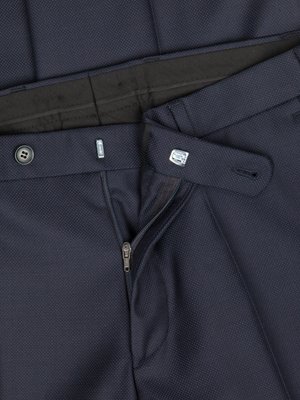 Close-up of blue trousers with visible texture, a button, a zipper, and two metallic clasps. The fly is partially unzipped. The belt loops are visible, along with the dark-colored waistband.