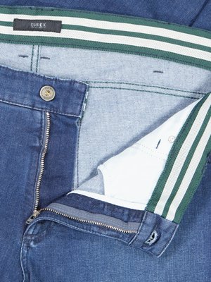 Nahaufnahme einer Jeanshose mit geöffnetem Reißverschluss und offenem Knopf. Auf dem Bund befindet sich ein Etikett mit der Aufschrift "EUREX". Ein grüner und weißer Streifen verläuft am Bund entlang. Die Hose ist blau.