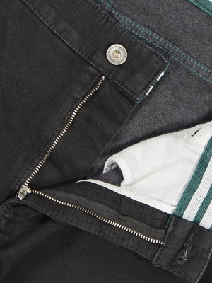 Nahaufnahme einer geöffneten schwarzen Jeanshose. Die Hose hat einen silbernen Reißverschluss, einen Knopf und grüne Nähte. Im Inneren ist weißer Stoff mit grünen Streifen sichtbar.