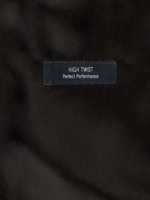 Close-up image of a dark fabric. A small, rectangular label, with rounded corners, is stitched onto the fabric. The label has two lines of white text that reads "HIGH TWIST" and "Perfect Performance."