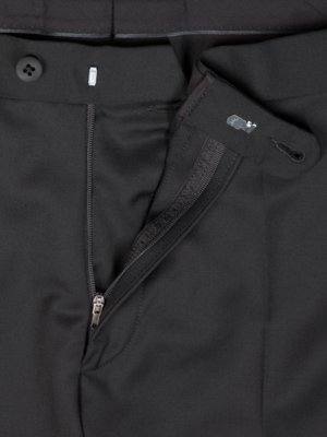 Close-up of black pants with a partially unzipped zipper. A button and a hook-and-eye closure are visible at the waist. The fabric shows subtle texture. The zipper pull and teeth are metallic.