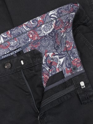 Nahaufnahme einer schwarzen Hose mit geöffnetem Hosenschlitz. Der Innenbund ist mit einem roten und blauen Paisley-Muster verziert. Sichtbar sind Knöpfe, ein Reißverschluss und das Innenfutter der Hose.