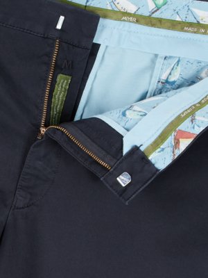 Nahaufnahme einer geöffneten Hose in Dunkelblau. Der Reißverschluss ist geöffnet und zeigt das Innere mit hellem blauem Futter und einem maritimen Muster. Ein Knopf und Etikett mit Größenangabe und Informationen.