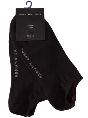 Schwarze Socken von Tommy Hilfiger. Über den Socken befindet sich ein Etikett, das mit einem blauen Haken aufgehängt ist. Das Etikett ist schwarz und hat den Markennamen und die Größenangaben. Die Socken haben einen roten Streifen.