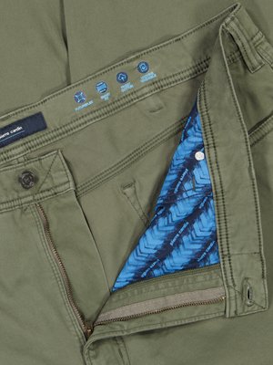 Detailní pohled na khaki kalhoty. Rozepnutý poklopec odhaluje modrou podšívku s bílým vzorem. Viditelný zip, knoflík a štítek s nápisem Pierre Cardin. Nad kapsou jsou grafické ikony.