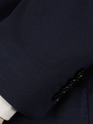 Close-up of a dark blue suit sleeve with three black buttons visible. A white shirt cuff is partially visible at the bottom left. The suit fabric has a visible textured pattern.