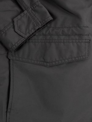 Close-up of a dark gray jacket detail. The image shows the jacket sleeve with a cuff and a button tab. Below the cuff, is a flap pocket with visible stitching.