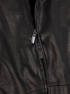 Nahaufnahme eines schwarzen Kleidungsstücks aus Leder. Der Reißverschluss ist teilweise geschlossen und aus Metall. Auf den Anhängern ist ein Markenzeichen eingraviert. Das Leder hat eine raue Textur mit sichtbaren Nähten entlang der Mitte.