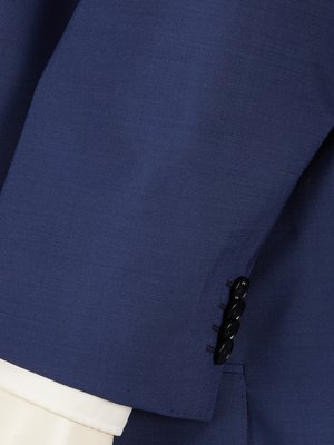 Close-up view of a navy blue suit jacket sleeve. Four black buttons are visible on the sleeve cuff. A white shirt cuff is visible underneath the jacket sleeve. The fabric of the jacket has a subtle texture.