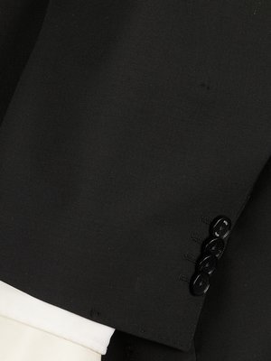 Close-up shot of a black jacket sleeve with three visible black buttons and a white shirt cuff partially visible at the bottom. The fabric texture of the jacket is visible.