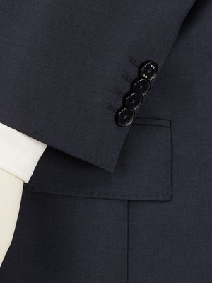 Close-up of a dark blue suit jacket sleeve. The sleeve features four black buttons. A white dress shirt cuff is visible under the jacket sleeve. The jacket has a pocket and stitching detail.