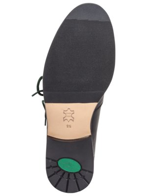 Ansicht von unten eines schwarzen Lederschuhs. Die Sohle besteht aus schwarzem, geriffeltem Gummi. Die Ferse ist hellbraun mit einem ledernen Symbol und der Größe 9 1/2. Grüne Schnürsenkel und ein grüner Kreis an der Sohle.