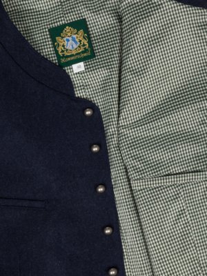Nahaufnahme einer dunkelblauen Weste mit metallfarbenen Knöpfen. Das Innenfutter ist grün-weiß kariert. Ein grünes Etikett mit goldfarbenem Wappen und Schriftzug "Hammerschmid" ist sichtbar. Größe 50.