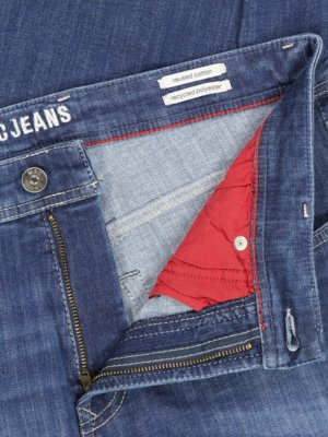 Nahaufnahme einer geöffneten blauen Jeanshose. Der Hosenlatz ist mit einem Reißverschluss geöffnet. Innenfutter aus rotem Stoff ist sichtbar. Auf der Jeans steht "C Jeans". Ein kleines Schild zeigt "reused cotton" und "recycled polyester".