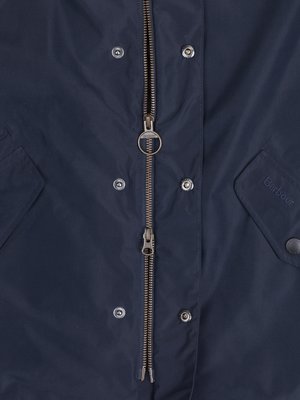 Nahaufnahme einer dunkelblauen Jacke mit Reißverschluss mittig. Knöpfe säumen den Reißverschluss. Zwei Taschen sind sichtbar, eine hat den Schriftzug "Barbour". Der Reißverschluss ist geöffnet.