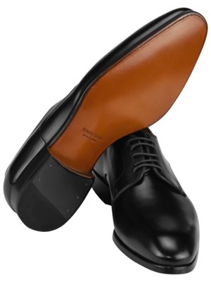 Zwei schwarze Lederschuhe, einer von unten gesehen, die Sohle aus braunem Leder, der andere mit Schnürsenkeln nach vorne gerichtet. Auf der Unterseite sind Markierungen zu sehen.