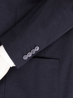 Nahaufnahme eines dunkelblauen Anzugsärmels, der die Ärmelknöpfe zeigt. Unten ist eine weiße Hemdmanschette zu sehen. Der Ärmel hat vier Knöpfe und eine aufgesetzte Tasche. Der Stoff hat eine feine Struktur.