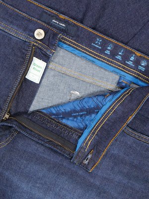 Nahaufnahme einer Jeans in Denim-Optik. Der Reißverschluss ist geöffnet, wodurch der Innenstoff mit blauem Muster sichtbar wird. Auf der Jeans befindet sich ein Etikett mit der Aufschrift "Green Rivet". Darüber befindet sich ein Knopf und ein Label mit "pierre cardin".