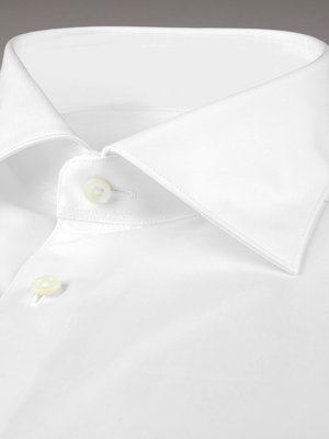 Nahaufnahme eines weißen Hemdkragens. Der Kragen ist spitz und hat zwei Knöpfe am Ausschnitt. Das Hemd ist aus glattem Stoff gefertigt und weist einen eleganten Schnitt auf. Der Hintergrund ist neutral.
