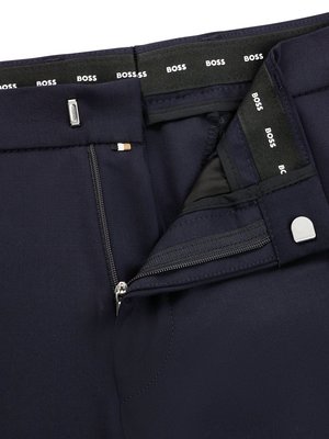 Nahaufnahme einer geöffneten marineblauen Hose. Der Reißverschluss ist offen. Über der Hose ist ein schwarzes Band mit dem Wort BOSS in weißen Buchstaben. Ein Metallknopf ist sichtbar.