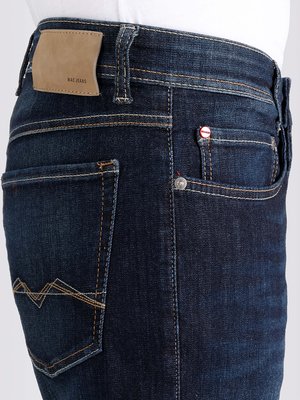 Nahaufnahme von dunkelblauen Jeans. Auf dem Gesäß sind zwei Taschen zu sehen, die eine mit einem Zickzack-Stich. Der Hosenbund hat einen lederartigen Aufnäher mit dem Markenlogo. Auf der rechten Seite ist eine kleine Tasche mit einem roten Knopf.