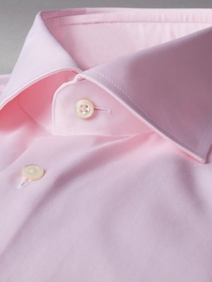 Nahaufnahme eines rosa Hemdkragens. Der Kragen ist geknöpft und hat eine helle Knopflochleiste. Zwei Knöpfe sind deutlich sichtbar. Der Stoff ist glatt und hellrosa. Die Nähte sind dezent.