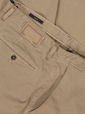 Nahaufnahme einer beigefarbenen Hose. Details sind Knopf, Hosentaschen, eine kleine Plakette mit Label, sowie der Hosenbund mit Gürtelschlaufen. Auf einem Label steht "slim fit". Der Stoff ist leicht gewebt.
