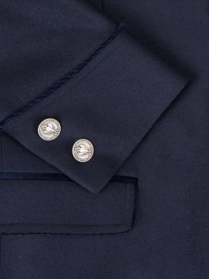 Nahaufnahme einer dunkelblauen Jacke mit zwei silbernen Knöpfen auf dem Ärmel. Der Stoff ist glatt und hat eine dunkle Farbe. Die Knöpfe sind rund und haben ein Relief. Die Jacke hat eine Tasche.