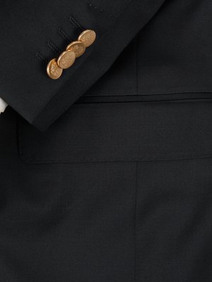 Nahaufnahme eines schwarzen Anzugs. Vier goldfarbene Knöpfe an einem Ärmel sind zu sehen, darunter eine angedeutete Taschenklappe. Der Stoff des Anzugs ist glatt.