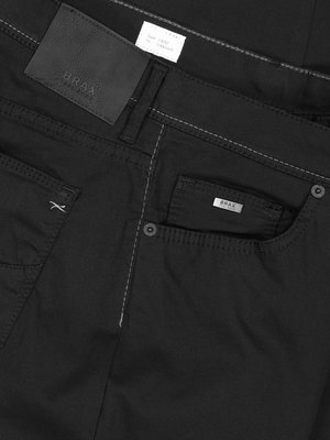 Nahaufnahme einer schwarzen Jeans mit sichtbaren Details: Gesäßtaschen, Münztasche mit silbernem "Brax"-Logo, weißer Naht und Leder-Label mit "Brax" Schriftzug. Details der Verarbeitung.