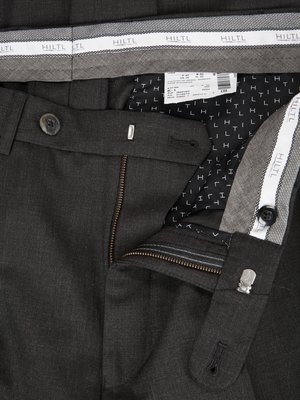 Nahaufnahme einer geöffneten grauen Herrenhose. Knopf, Reißverschluss und Hosenbund mit HILTL-Schriftzug sind sichtbar. Auf der Innenseite ist ein schwarzes Muster mit weißen "H" und "T" Buchstaben zu sehen.