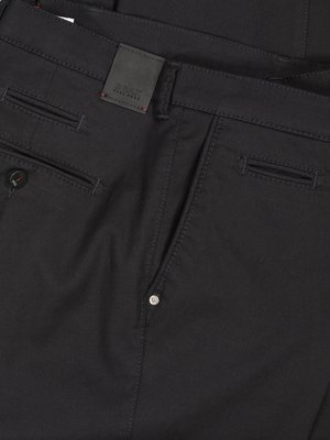 Nahaufnahme einer grauen Hose. Der Fokus liegt auf der Vorderseite mit Knopftasche, Reißverschluss, Knopf und einem kleinen Lederetikett am Bund. Detailreiche Nähte sind sichtbar.