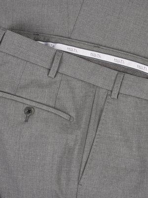 Nahaufnahme einer grauen Hose. Der Bund ist sichtbar, mit Gürtelschlaufen und einem Schild mit der Aufschrift "HILTL". Die Hosentasche und ein Knopf sind auch deutlich zu sehen. Die Hose ist aus Stoff.