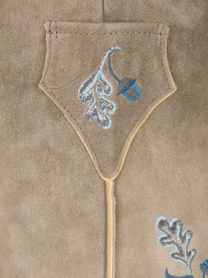 Nahaufnahme eines beigefarbenen Leders mit aufgesticktem Eichenblatt und Eichel in Hellblau und Grau auf einer Tasche. Unterhalb der Tasche, am rechten Rand, ist ein weiteres Blatt zu sehen. Ein gelber Zierstreifen umrandet die Tasche.