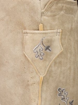 Nahaufnahme von hellem Leder, vermutlich von einer Hose oder einem Rock. Eine kleine Tasche mit besticktem Blattmuster ist sichtbar. Das Leder ist an den Nähten und mit hellgrauer Stickerei verziert. Das Bild zeigt die detaillierte Textur des Leders.