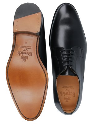 Ansicht von oben von zwei schwarzen Lederschuhen. Einer zeigt die Sohle mit Logo und Größenangabe. Der andere Schuh ist mit Schnürsenkeln versehen, ebenfalls aus Leder, mit Logo auf der Einlegesohle.