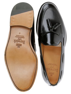 Zwei schwarze Lederschuhe, Draufsicht. Der linke Schuh zeigt die Ledersohle, die mit der Marke Berwick versehen ist. Der rechte Schuh zeigt eine glänzende Oberfläche und eine Quaste. Das Innenfutter beider Schuhe ist hellbraun.