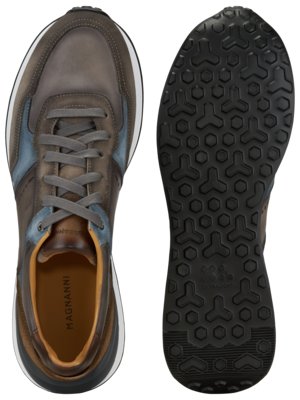 Zwei Ansichten eines Schuhs auf weißem Hintergrund. Der linke Schuh ist braun mit blauen Akzenten und grauen Schnürsenkeln. Die Sohle ist weiß. Der rechte Schuh zeigt die schwarze Unterseite mit einem geometrischen Muster.