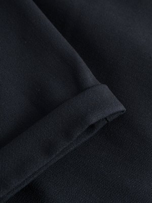 Nahaufnahme eines gefalteten, dunkelblauen Stoffes, möglicherweise ein Ärmel oder Saum. Die Textur des Stoffes ist deutlich erkennbar. Der gefaltete Bereich bildet eine dicke Linie am linken Bildrand. Der Stoff selbst ist glatt.