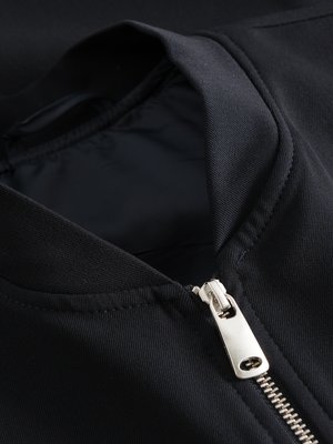 Nahaufnahme einer schwarzen Jacke mit einem hochgezogenen Reißverschluss. Der Reißverschluss ist silberfarben und glänzend. Die Jacke hat einen schwarzen Kragen. Der Innenstoff ist dunkelblau.