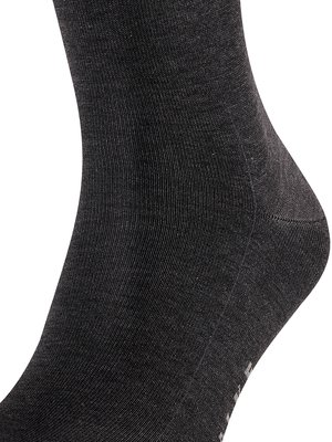 Nahaufnahme eines schwarzen Strumpfes aus Stoff, die Ferse und ein Teil des Fußes sind sichtbar. Der Stoff ist feinmaschig gewebt und leicht texturiert. Die Farbe ist dunkelgrau.